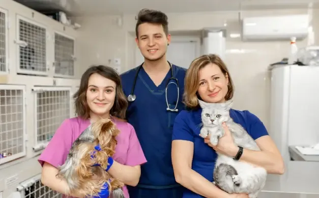 tres médicos veterinarios, sostienen dos animales mientras miran hacia en frente 